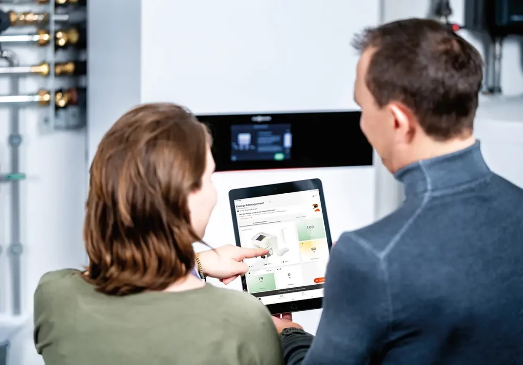 Paar steht vor einer Wärmepumpe und hält ein Tablet mit geöffneter VIESSMANN VICARE App in der Hand