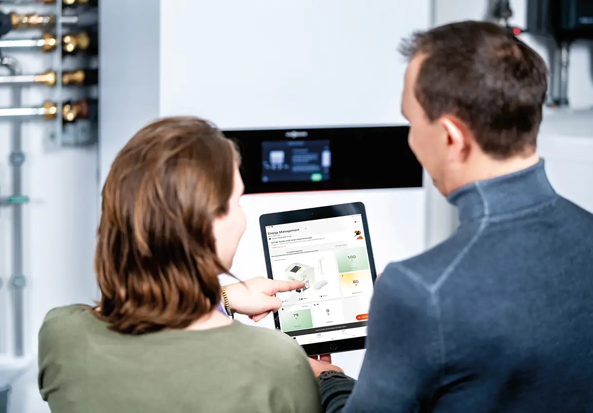 Paar steht vor einer Wärmepumpe und hält ein Tablet mit geöffneter VIESSMANN VICARE App in der Hand