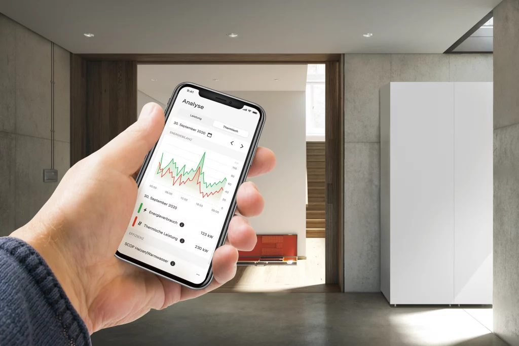 Geöffnete ViCare-Energiemanagement-App auf dem Handy eines MAnnes, der vor einem Stromspeicher in einem Haus steht.